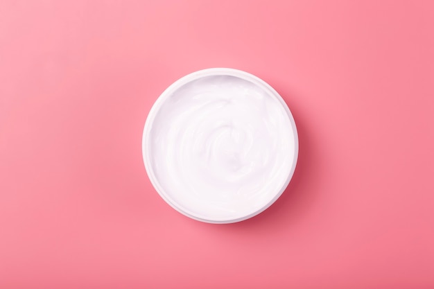 Cosmetische crème achtergrond witte cosmetische crème voor huid en lichaam in een open witte pot op een roze lege...