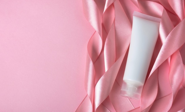 Cosmetische crème tube verpakking met zijden lint op roze achtergrond Schoonheid huidverzorging