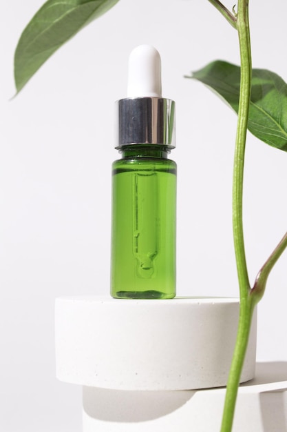 Cosmetische fles met druppelaar op podium Serumcontainer en planttakjes op witte achtergrond Biologische cosmetica schoonheidsproducten concept