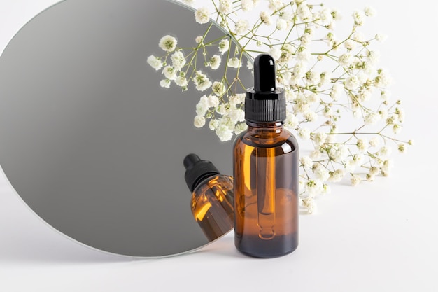 Cosmetische fles met een druppelaar op de achtergrond van een spiegel en gypsophila serum-essentieolie voor gezichtsverzorging natuurlijke biologische cosmetica