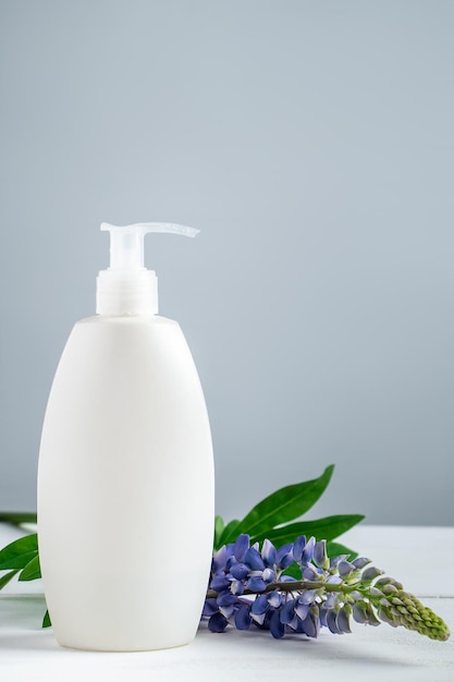 Cosmetische fles met lotion en lupine bloemen op grijze achtergrond