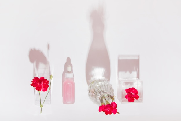 Cosmetische fles met pipet en roze vloeistof omringd door roze bloemen op een lichte achtergrond