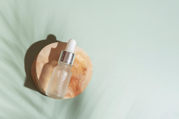 Cosmetische fles met pipet op houten plak bovenaanzicht plat lag op gekleurde achtergrond met palmschaduw Natuurlijk cosmetisch concept