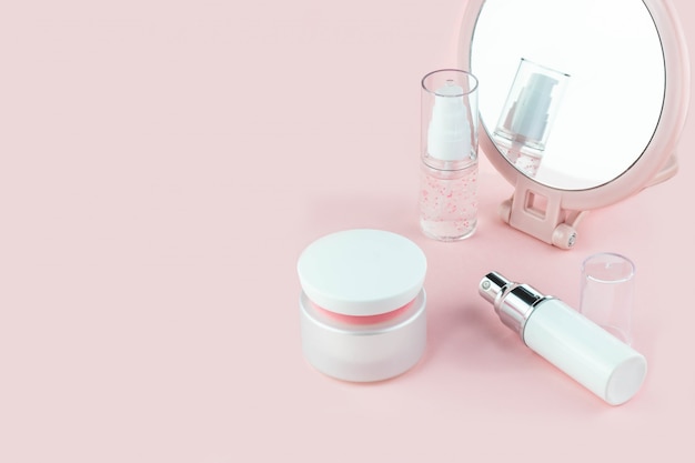 Cosmetische flessen met serum, gel, gezichtscrème op een roze achtergrond met een spiegel. Huidcosmetica, minimalisme