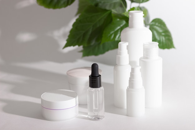 Cosmetische flessen staan naast groene bladeren op een witte achtergrond. Biologisch cosmetica concept