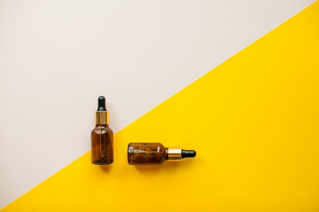 Cosmetische flessen voor serumolie of crème op felgele en lichtroze achtergrond