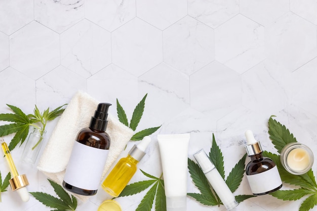 Cosmetische flessenpotten en tubes met blanco label in de buurt van groene cannabisbladeren bovenaan Mockup