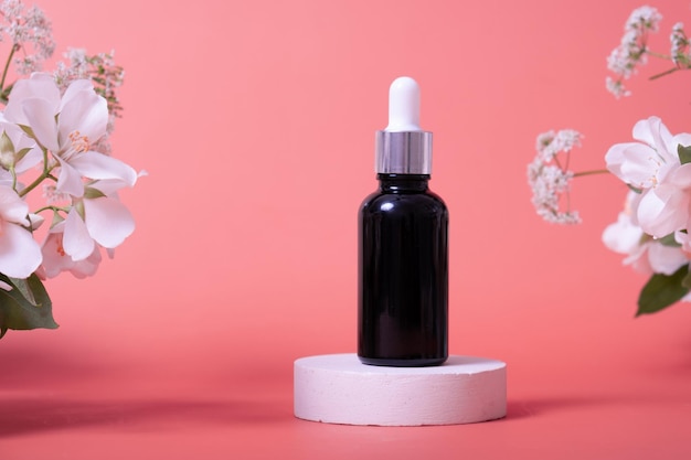 Cosmetische glazen druppelflesje met olieserum of fruitpeeling op podium met jasmijnbloemen schoonheid