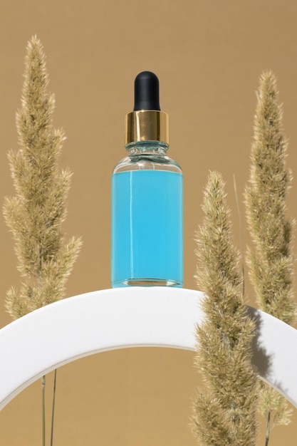 Cosmetische glazen fles met druppelaar voor etherische oliën en serum op een podium met droog pampagras Gezichts- en lichaamsverzorging spa-concept en natuurlijke cosmetica