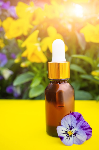 Cosmetische glazen fles met een pipet op de ruimte van een struik met altvioolbloemen. Concept voor natuurlijke biologische cosmetica, oliën, aromatherapie, spa, eco, bio.