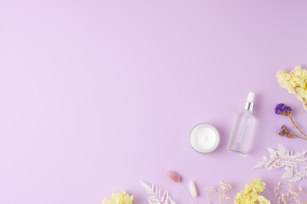 Cosmetische huidverzorgingsproducten met bloemen op roze achtergrond Plat lag kopieerruimte