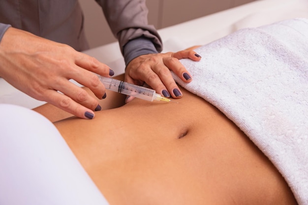 Cosmetische injectie in de spa salon. Schoonheidsspecialiste maakt injectie in de buik van de patiënt. het begrip verjonging.