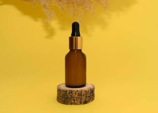 Cosmetische olie in een glazen fles staat op een houten podium Riet op een gele achtergrond