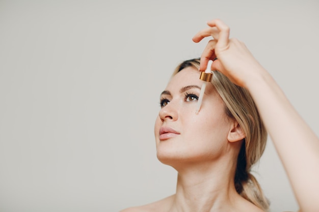 Cosmetische olie koninginnengelei aanbrengen met pipet op gezicht van jonge volwassen vrouw