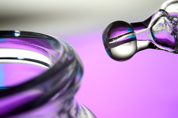 Cosmetische pipet met druppels transparante vloeistof en een pot, close-up op een gekleurde achtergrond.