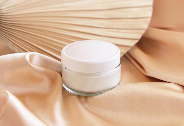 Cosmetische pot met wit deksel op beige satijnen stof en gedroogd palmblad close-up mockup