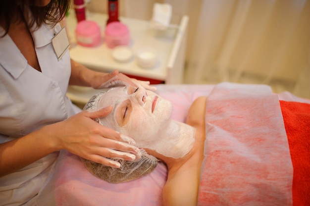 Cosmetische procedure met een wit masker op een jonge vrouwelijke gezicht close-up.