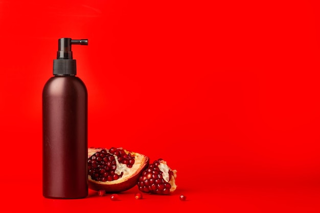 Cosmetische spuitfles met plakjes granaatappel op rode achtergrond