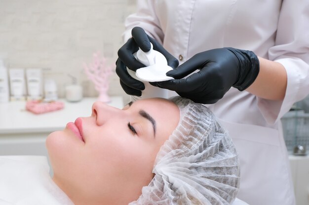 Cosmetologie. Close-up foto van mooie jonge vrouw met gesloten ogen die gezichtsreinigingsprocedure in schoonheidssalon ontvangt.