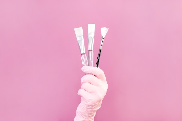 Cosmetologie concept, schoonheidsspecialiste in de hand zijn borstels, roze achtergrond