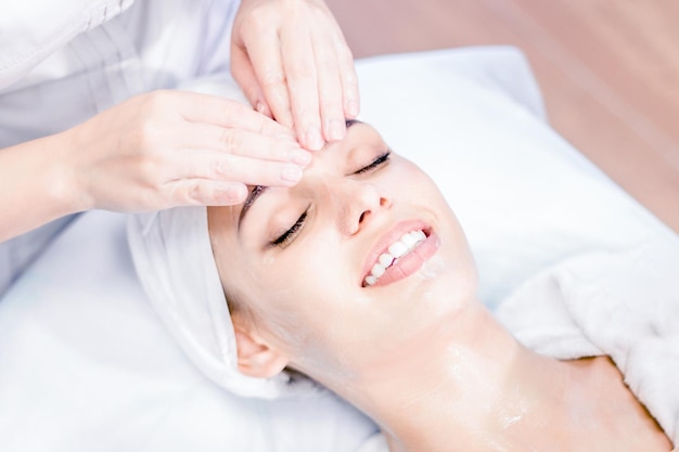Cosmetologie de handen van een schoonheidsspecialist doen een gezichtsmassage met een masker glimlachend meisje op spa-procedure gezichtsbehandeling