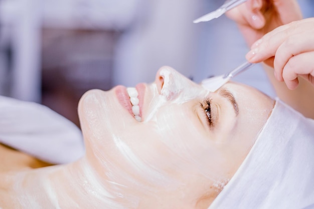 Cosmetologie De schoonheidsspecialist past een reinigend gezichtsmasker toe Glimlachend meisje op de procedure voor gezichtsverjonging