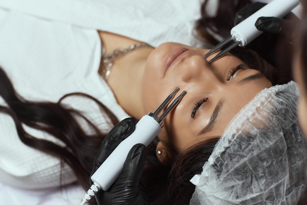 Cosmetologie. Mooie vrouw in de spa-kliniek die stimulerende elektrische gezichtsbehandeling van de therapeut ontvangt.