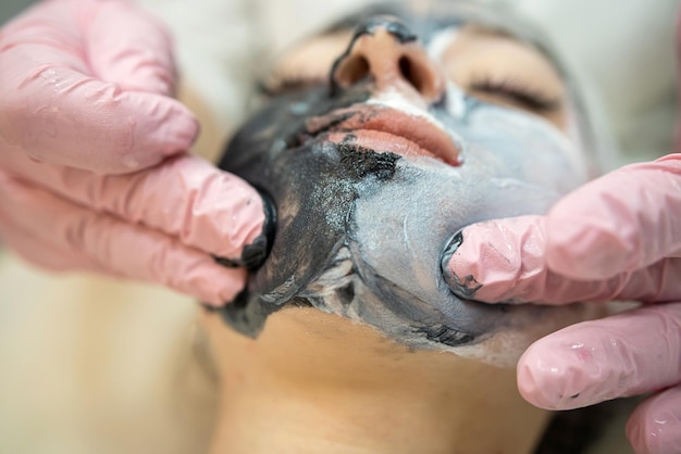 косметолог наносит маску на лицо клиента и выполняет массаж подъема лица