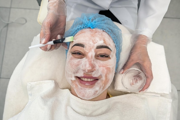 Cosmetologist applies a black mask on the face of a pretty woman in black gloves