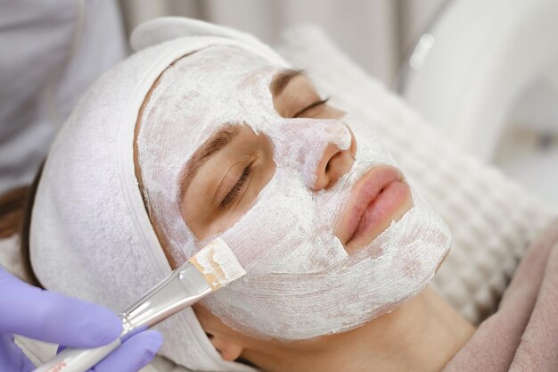 Photo cosmetologist apply skin mask with brush care and treatment procedure in modern aesthetic clinic