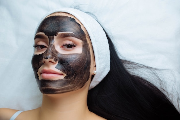 Photo cosmetologist applying black mask on pretty woman face wearing black gloves gorgeous woman in spa h