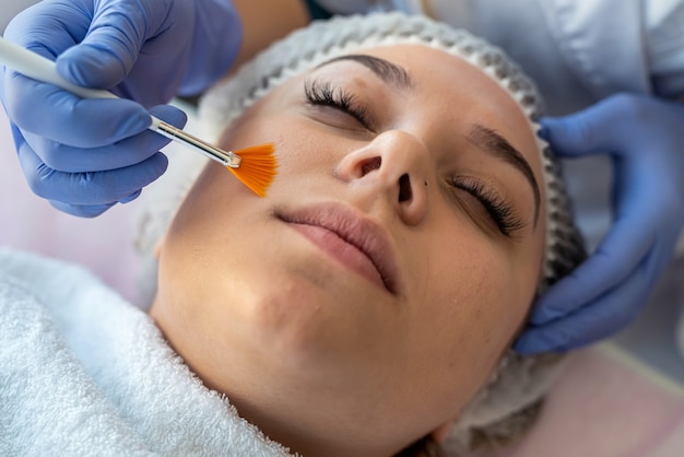 Cosmetologist applying  healing cream on female client face skin in beauty clinic. healthcare