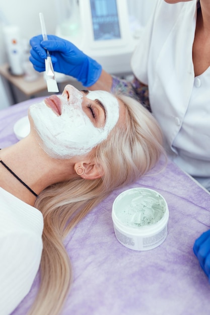 Cosmetologist applying mask on clients face in spa salon