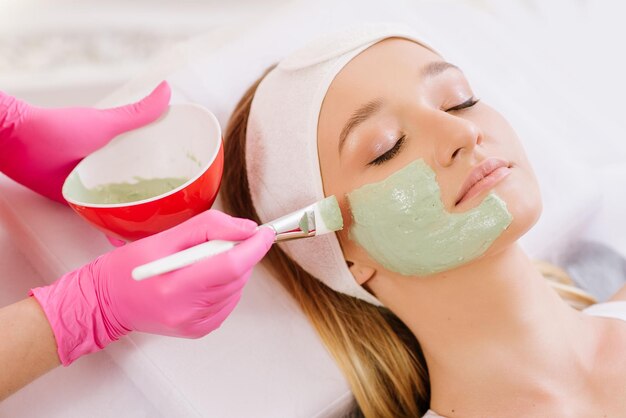 Cosmetologist applying mask on face of  woman in spa salon