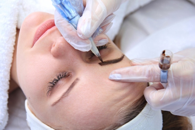 Photo cosmetologist applying permanent make up on eyebrows- eyebrow tattoo