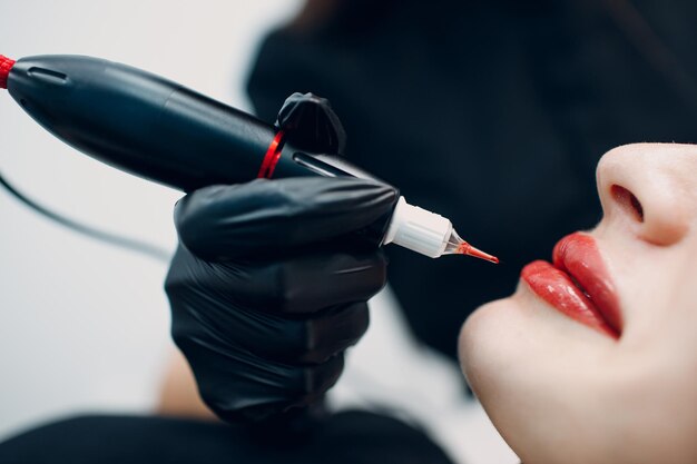 若い女性の唇に赤いアートメイクタトゥーを適用する美容師
