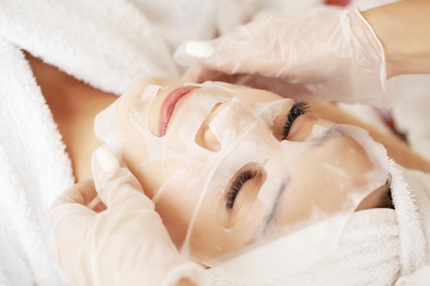 Cosmetologo che applica una maschera in tessuto sulla donna nel salone termale