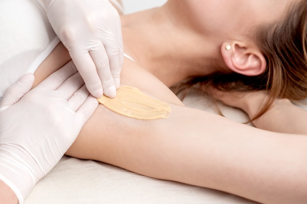 Photo cosmetologist applying wax paste on armpit