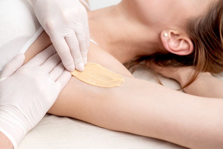 Cosmetologist applying wax paste on armpit