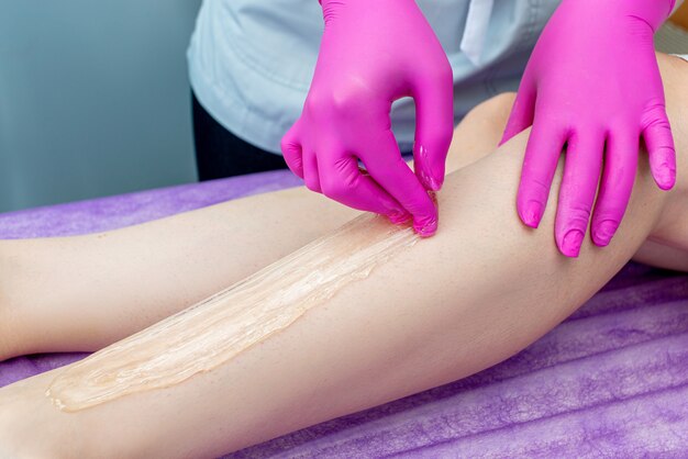 Cosmetologist beautician waxing female legs in a beauty salon