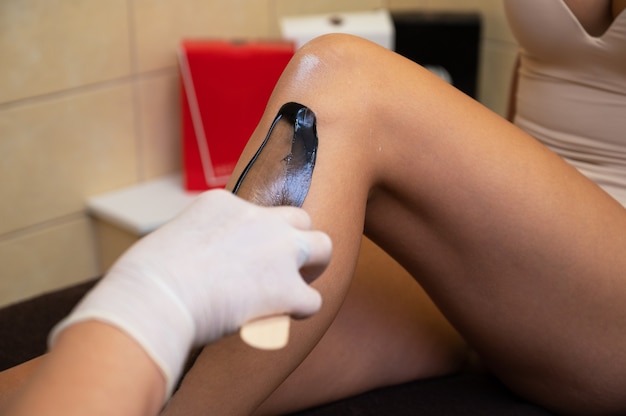 Cosmetologist in beauty clinic performs a epilation procedure for removing hair from the female leg ...