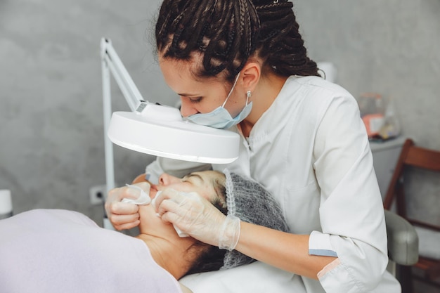 A cosmetologist cleanses the face under a cosmetic magnifying\
glass the concept of cosmetology a cosmetologist performs a facial\
cleansing procedure with problem skin