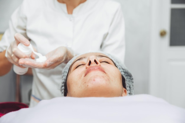 Il cosmetologo deterge la pelle con la schiuma una procedura per la cura della pelle di una donna cosmetici naturali un bel viso trattamento cosmetico del viso crema peeling terapeutica