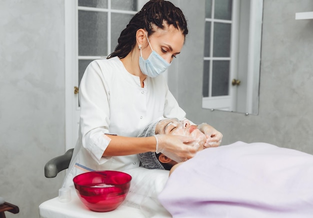 Il cosmetologo deterge la pelle con la schiuma una procedura per la cura della pelle di una donna cosmetici naturali un bel viso trattamento cosmetico del viso crema peeling terapeutica