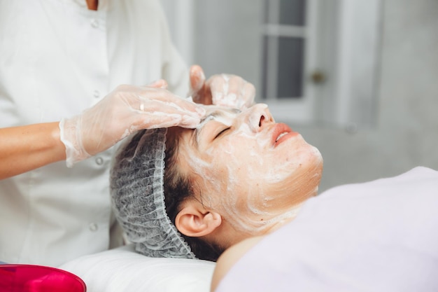 The cosmetologist cleanses the skin with foam A woman's skin care procedure Natural cosmetics A beautiful face Cosmetic treatment of the face Therapeutic peeling cream