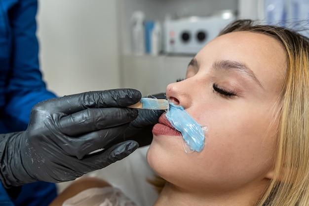 Foto un medico cosmetologo applica la cera depilatoria sul labbro di una giovane cliente per rimuovere i peli indesiderati