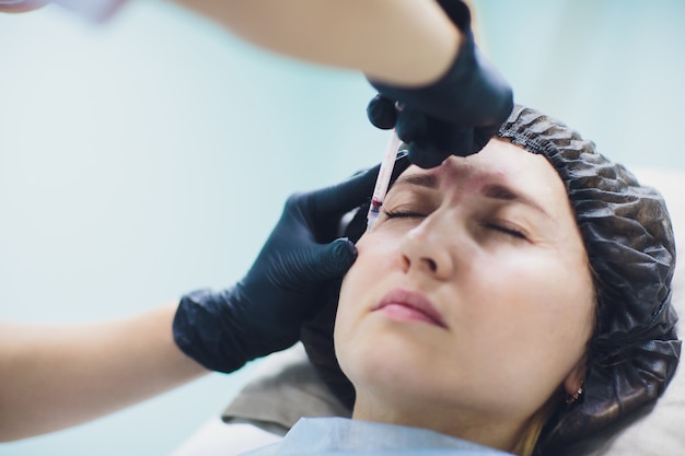 Cosmetologist doctor make facial beauty injections to her woman client. Beautiful female face and cosmetologist's hands with syringe. Rejuvenation and hydratation. Cosmetology concept in clinic.