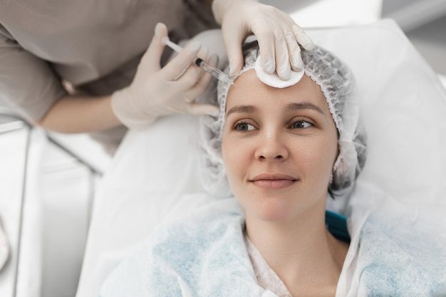 Cosmetologist doctor with a syringe in his hand makes injections in the forehead of the client's face