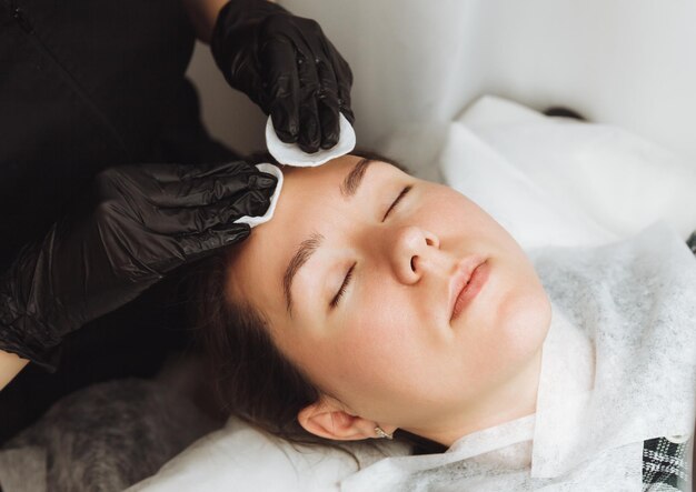 Косметолог делает косметический массаж лица для лица расслабленной молодой женщины в салоне красоты