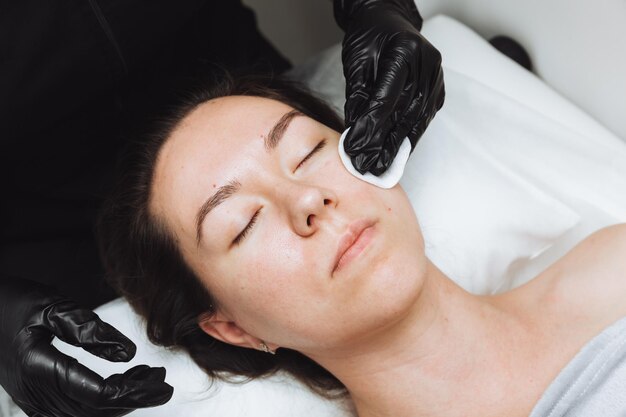 Косметолог делает косметический массаж лица для лица расслабленной молодой женщины в салоне красоты